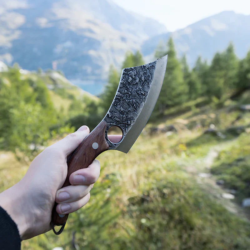 Hand holding the Loki knife in the wild, highlighting the blade against scenic mountain views.